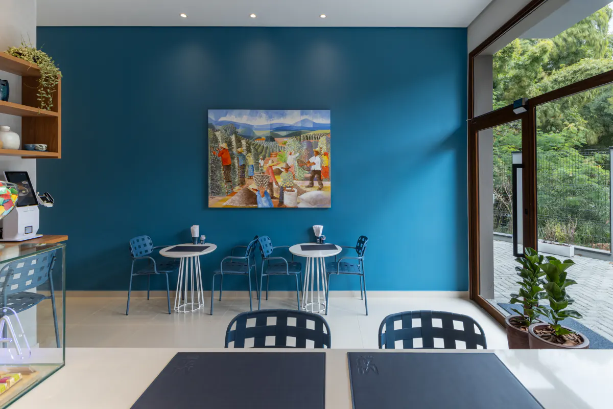 Salão da cafeteria do LYRATA com mesas, parede azul e obra de arte
