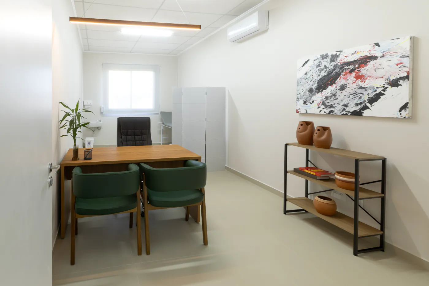 Consultório médico do LYRATA com mesa de atendimento, obra de arte e estante
