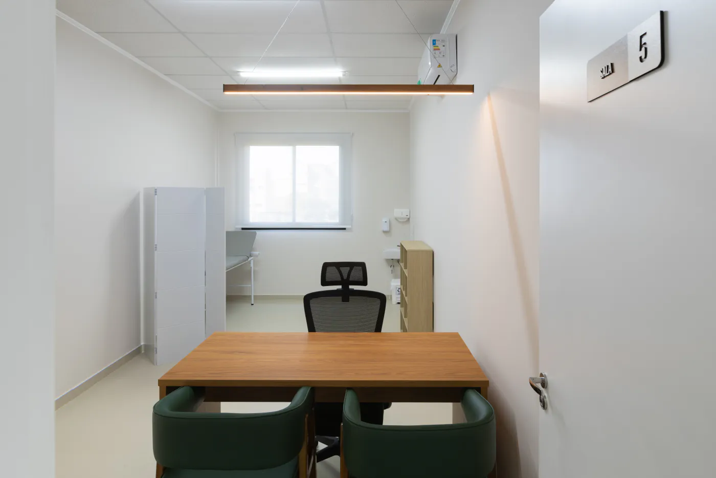 Sala multidisciplinar do LYRATA, com mesa de atendimento, maca e biombo